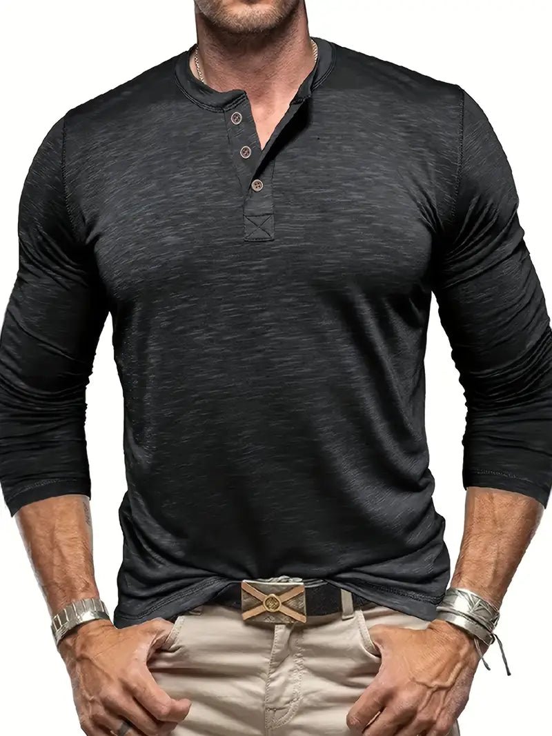 Mann in schwarzem Henley-Shirt mit langen Ärmeln und beiger Hose, trägt Armbänder und Gürtel. Modische Herrenbekleidung, lässiger Stil.