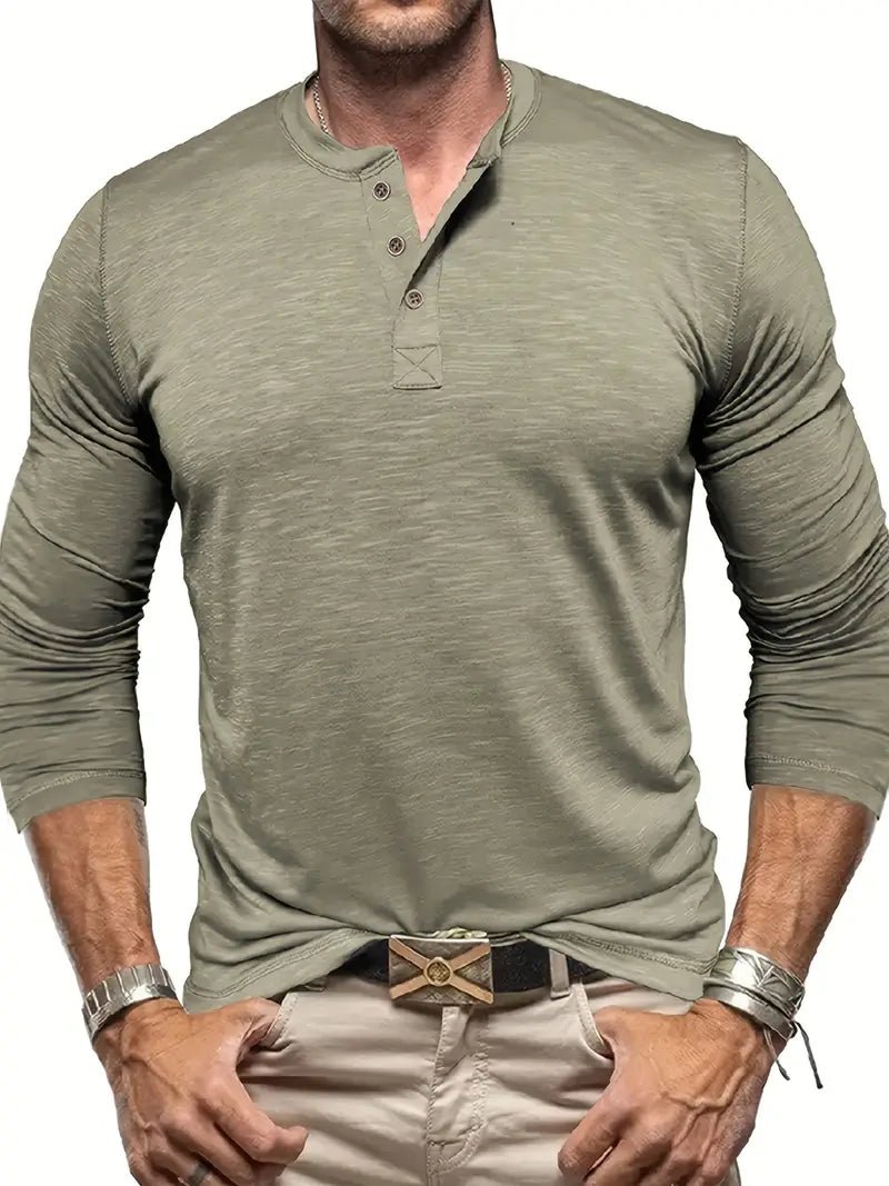 Mann in olivgrünem Henley-Shirt mit langen Ärmeln, beige Hose und Lederarmbändern. Modischer Freizeitlook für Herren.
