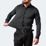Mann in schwarzem, elastischem Hemd zieht am Stoff, um Flexibilität zu demonstrieren. Modische Herrenbekleidung, dehnbares Material, elegantes Design.
